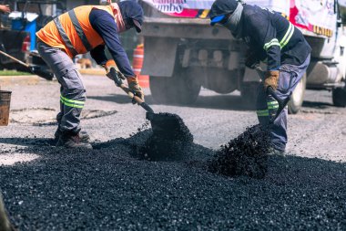 Puebla sokaklarında çukur açmak için asfalt döşeyen iki işçi.