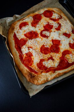  Erimiş peynirli gurme pepperoni pizza ve çıtır çıtır ekmek, ince ve zarif atmosferdeki zengin renk ve dokularını vurgulayarak koyu gıda tarzında sunuluyor.