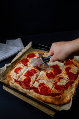  Erimiş peynirli gurme pepperoni pizza ve çıtır çıtır ekmek, ince ve zarif atmosferdeki zengin renk ve dokularını vurgulayarak koyu gıda tarzında sunuluyor.
