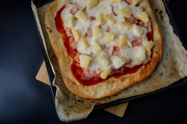 Erimiş peynirli, ananaslı ve jambonlu bir gurme Hawai pizzası koyu gıda tarzında sunuluyor, ince ve zarif bir atmosferde karşıtlıkları ve dokuları vurguluyor.