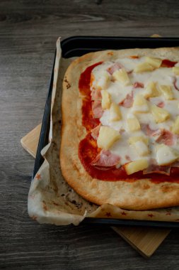 Erimiş peynirli, ananaslı ve jambonlu bir gurme Hawai pizzası koyu gıda tarzında sunuluyor, ince ve zarif bir atmosferde karşıtlıkları ve dokuları vurguluyor.