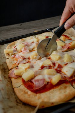 Erimiş peynirli, ananaslı ve jambonlu bir gurme Hawai pizzası koyu gıda tarzında sunuluyor, ince ve zarif bir atmosferde karşıtlıkları ve dokuları vurguluyor.