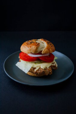 Siyah tabakta salatalık, domates ve marullu sığır burger, koyu besin estetiği ve karamsar arkaplan, dikey formatta yakalanır.