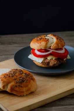 Siyah tabakta salatalık, domates ve marullu sığır burger, koyu besin estetiği ve karamsar arkaplan, dikey formatta yakalanır.