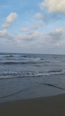 Uçsuz bucaksız okyanus ve boş bir plajın sakin bir videosu. Mavi gökyüzünün altında, bulutlu, yumuşak dalgalar kırılıyor..