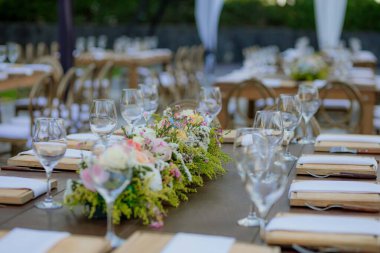 Kristal bardaklar ve çiçekli süslemelerle süslenmiş ahşap masa, bir düğün ya da zarif bir kutlama için açık havada hazırlanır..