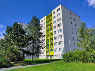 Prag, Çek Cumhuriyeti - 16 Temmuz 2022: Önünde yeşil şeritli ve kozalaklı ağaçlar bulunan güzel yenilenmiş eski apartman blokları.