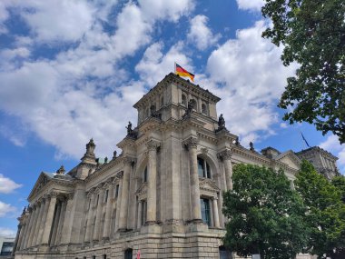 Berlin, Almanya - 4 Temmuz 2022: Kulenin tepesinde büyük Alman bayrağı olan Alman Bundestag 'ının köşesi. Arka planda gökyüzünde güzel mavi bulutlar var..