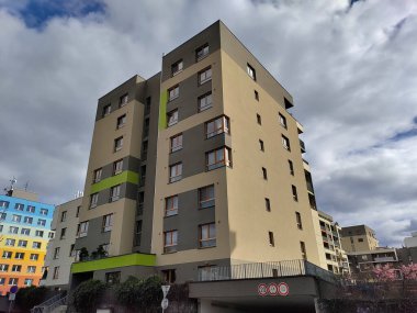 Prag, Çek Cumhuriyeti - 1 Nisan 2023: Üzerinde yeşil çizgiler bulunan bej ve gri cepheli modern apartman binası. Hava bulutlu..