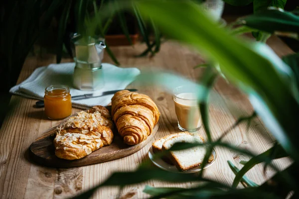 与羊角面包和咖啡共进早餐 餐桌上满是美丽的植物 享受家庭生活的乐趣 — 图库照片