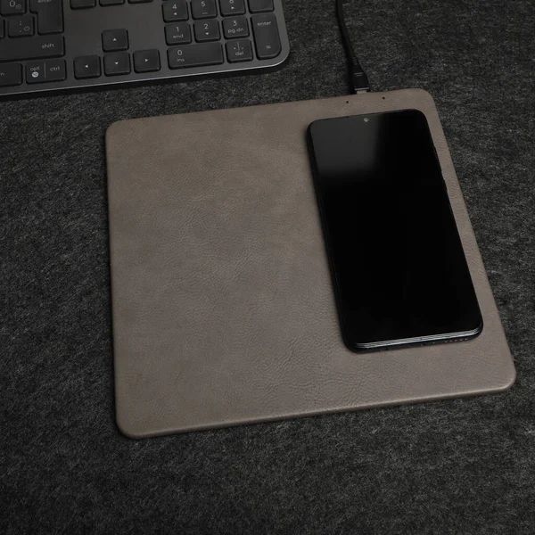 Charging the smartphone with leather wireless charger on desk. Colorful leather charger pads. Wireless mousepad, Charger pad. Closeup, top view, no people. Concept shoot.