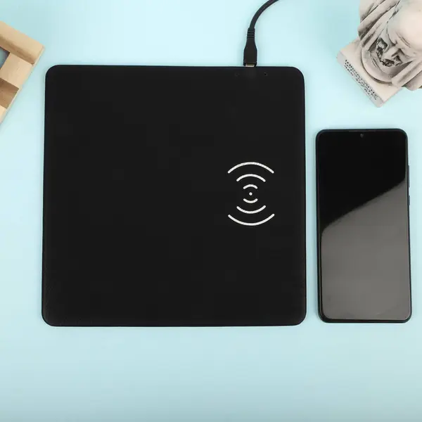 Charging the smartphone with leather wireless charger on desk. Black leather charger pads. Wireless mousepad, Charger pad. Closeup, top view, no people. Concept shoot.
