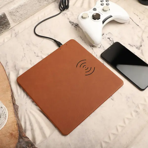 Charging the smartphone with leather wireless charger on desk. Light brown leather charger pads. Wireless mousepad, Charger pad. Closeup, top view, no people. Concept shoot.