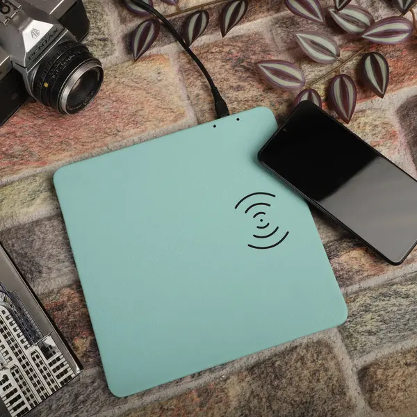 Charging the smartphone with leather wireless charger on desk. Teal leather charger pads. Wireless mousepad, Charger pad. Closeup, top view, no people. Concept shoot.
