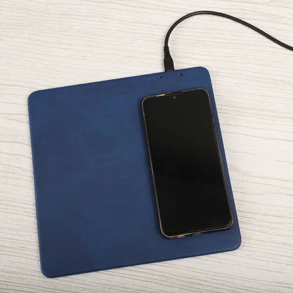 Charging the smartphone with leather wireless charger on desk. Blue leather charger pads. Wireless mousepad, Charger pad. Closeup, top view, no people. Concept shoot.