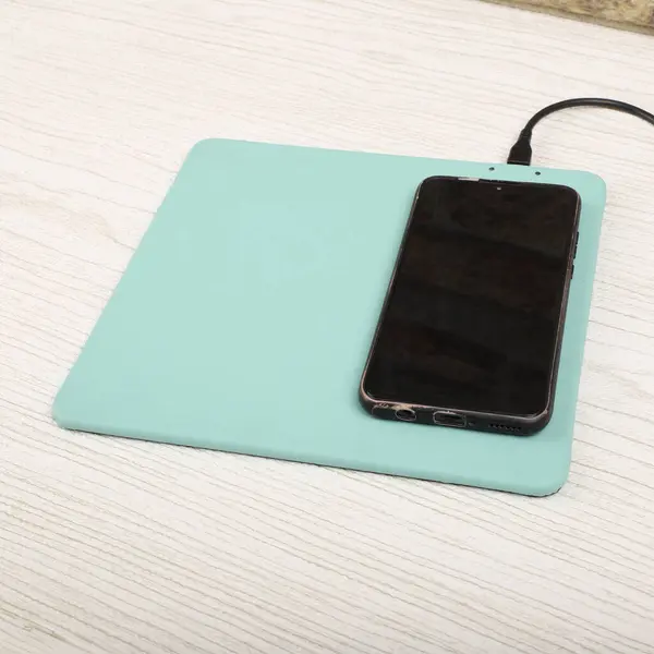 Charging the smartphone with leather wireless charger on desk. Teal