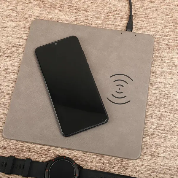 Charging the smartphone with leather wireless charger on desk. Gray leather charger pads. Wireless mousepad, Charger pad. Closeup, top view, no people. Concept shoot.