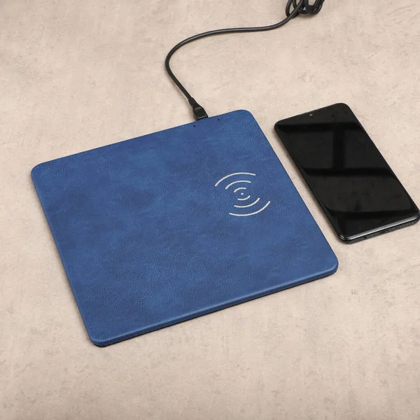 Charging the smartphone with leather wireless charger on desk. Blue leather charger pads. Wireless mousepad, Charger pad. Closeup, top view, no people. Concept shoot.