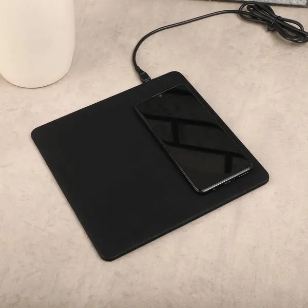 Charging the smartphone with leather wireless charger on desk. Black leather charger pads. Wireless mousepad, Charger pad. Closeup, top view, no people. Concept shoot.