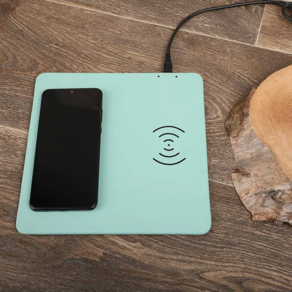 Charging the smartphone with leather wireless charger on desk. Teal leather charger pads. Wireless mousepad, Charger pad. Closeup, top view, no people. Concept shoot.