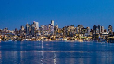 Seattle 'ın şehir merkezindeki ufuk çizgisinin geniş bir görüntüsü mavi saat boyunca, Parıldayan şehir ışıkları Lake Union' un sakin sularına yansıyor. Bu görüntü Seattle 'ın modern mimarisini ve canlı gece hayatını vurgular..
