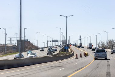 Gündüz vakti köprüden geçen çok şeritli bir otoyolda ılımlı trafiği gösteren yüksek çözünürlüklü bir görüntü. Sokak lambaları otoyolda ve yön işaretleri görülebiliyor, bu da onu ulaşım, altyapı veya seyahat temaları için ideal hale getiriyor..