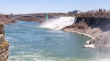 Niagara Şelalesi 'ndeki Amerikan Şelalesi' nin nefes kesici geniş açılı görüntüsü, arkada Kanada ve ABD 'yi birbirine bağlayan Gökkuşağı Köprüsü. Gözlem kulesi, şelalenin yanında yükselmekte. Güçlü çağlayandan yükselen sis gibi.. 