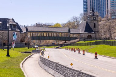 Niagara Şelalesi, Ontario yakınlarındaki tarihi taş binaların yanından geçen manzaralı bir yolun canlı fotoğrafı. Mimaride bir saat kulesi ve arka planında modern gökdelenlerin yükseldiği bir yaya köprüsü yer alıyor..