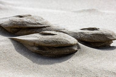 Kıyı kum tepelerindeki rüzgar şeklindeki kum oluşumlarının yakın görüntüsü. Bu doğal soyut yapılar organik dokuları ve erozyon kalıplarını sergiliyor, onu arka planda, güzel sanatlarda, jeolojide ve tasarım projelerinde kullanılmak üzere mükemmel hale getiriyor..