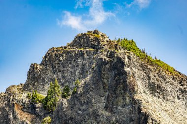 Göz kamaştırıcı bir dağ zirvesi, dağınık bulutlarla dolu canlı mavi gökyüzünün altında, yemyeşil ormanların üzerinde yükseliyor. Bu manzaralı manzara doğanın güzelliğini yakalar ve seyahat, macera, yürüyüş ve fotoğrafçılık veya tasarım alanlarında açık hava temaları için idealdir..