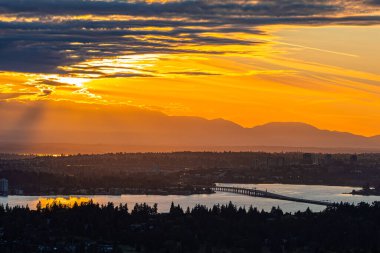 Bu çarpıcı fotoğraf Seattle 'daki Washington Gölü üzerinde altın bir günbatımını yakalar, ikonik yüzen köprü, parlayan gökyüzü, siluetli ağaçlar ve uzak dağ tepeleri. Seyahat, doğa, manzara ve Pasifik' in kuzeybatısında stok kullanımı için idealdir..