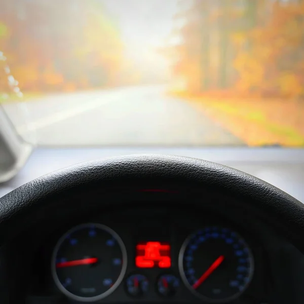 Car interior with dashboard on wet road in autumn season. Foggy and dangerous driving - concept for traffic and road safety - view from the driver\'s seat.