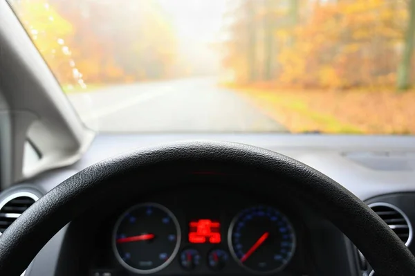 Car interior with dashboard on wet road in autumn season. Foggy and dangerous driving - concept for traffic and road safety - view from the driver\'s seat.