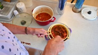 Kırmızı gömlekli yaşlı adam kaşıkla çorba yapıyor..