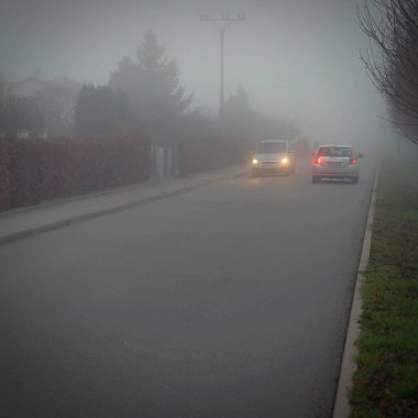 Car traveling on the foggy road with headlights or headlamps on. Low visibility - Dangerous driving of cars in winter in bad weather