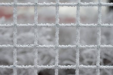 A minimalist close-up of a frosted metal grid, delicately coated in ice crystals, set against a soft, blurred winter background. The intricate patterns of the frost highlight the geometric symmetry of the grid, creating a serene and abstract winter c clipart