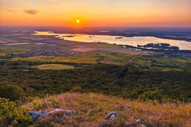 Devin Dağı 'ndan güzel bir gün batımı. Çek Cumhuriyeti, Güney Moravya 'daki Palava Tepeleri' nin çarpıcı panoramik manzarası. Manzarada kayalık üzüm bağları, kayalık uçurumlar, yemyeşil ormanlar ve altın saatinde turuncu bir yaz gökyüzü yer alıyor.. 