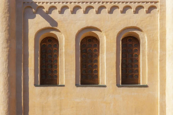 Three antique window frames with round window panes on a yellow wall. Old windows with small circular glass in wooden frames. Openings in the wall, round arches, and columns on the yellow facade