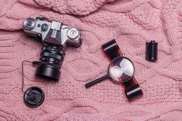 An old retro camera, photographic film and a magnifying glass lie on a pink wool sweater.