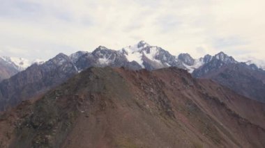 Kayalıklardan yaklaşıyor, arkasında karlı bir tepe var. Bulutlu hava