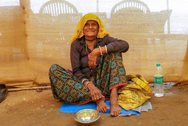 GOA, Hindistan - 22 Şubat 2024: Fakir bir kadın yüzünde bir gülümsemeyle yerde oturan sadaka topluyor.
