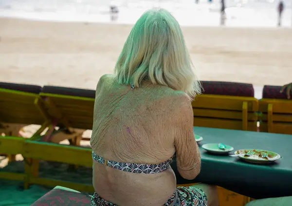 stock image GOA, India - February 18, 2024: Wrinkled skin back of an old lady sitting on the beach. Travel time