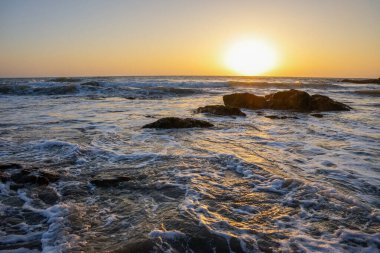 Denizin köpüklü dalgaları ve batan güneşin yansıması. Rahatlama