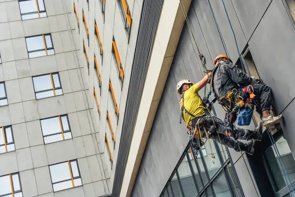 Almaty, Kazakistan - 14 Temmuz 2025: Endüstriyel tırmanışçılar binanın ön cephesini onarıyor. Yüksek irtifa çalışması                            