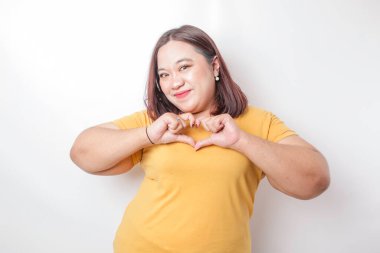 Sarı tişört giyen çekici, Asyalı, iri yarı bir kadın mutlu ve romantik şekilli bir kalp hareketi şefkatli duygular ifade eder.