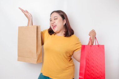 Mutlu, genç, Asyalı, iri yarı bir kadın sarı gömlek giyiyor ve elinde hediye kutusu ve alışveriş çantası tutuyor..