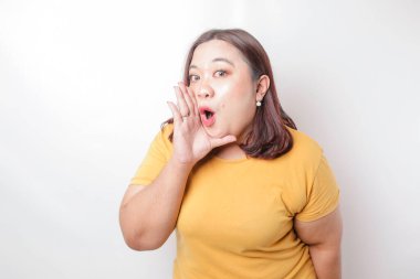 Sarı tişörtlü, genç, güzel, Asyalı, iri yarı bir kadın ağzında bir eliyle bağırıyor ve çığlık atıyordu. iletişim konsepti.