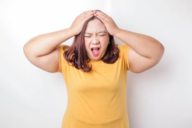 Beyaz arka planda izole edilmiş sarı tişört giyen Asyalı iri bir kadının portresi depresif görünüyor.