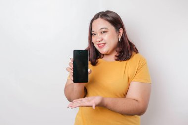 Mutlu bir Asyalı kadın portresi gülümsüyor ve akıllı telefonunda beyaz bir arka planla izole edilmiş sarı tişört giyen bir fotokopi çekiyor.