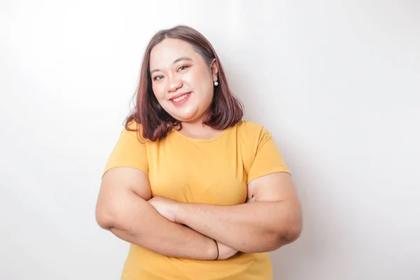 一个有自信的笑着的大个子亚洲女人的画像 她穿着黄色的衬衫 双臂交叉地站在一起 看着被白色背景隔开的相机 — 图库照片